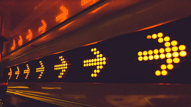 A series of glowing arrow signs in a city environment, indicating direction at night.